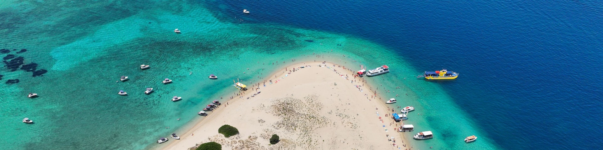 An aerial view of a beach with clear turquoise waters, surrounded by dense green vegetation.