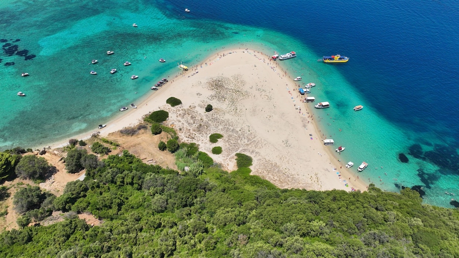 An aerial view of a beach with clear turquoise waters, surrounded by dense green vegetation.