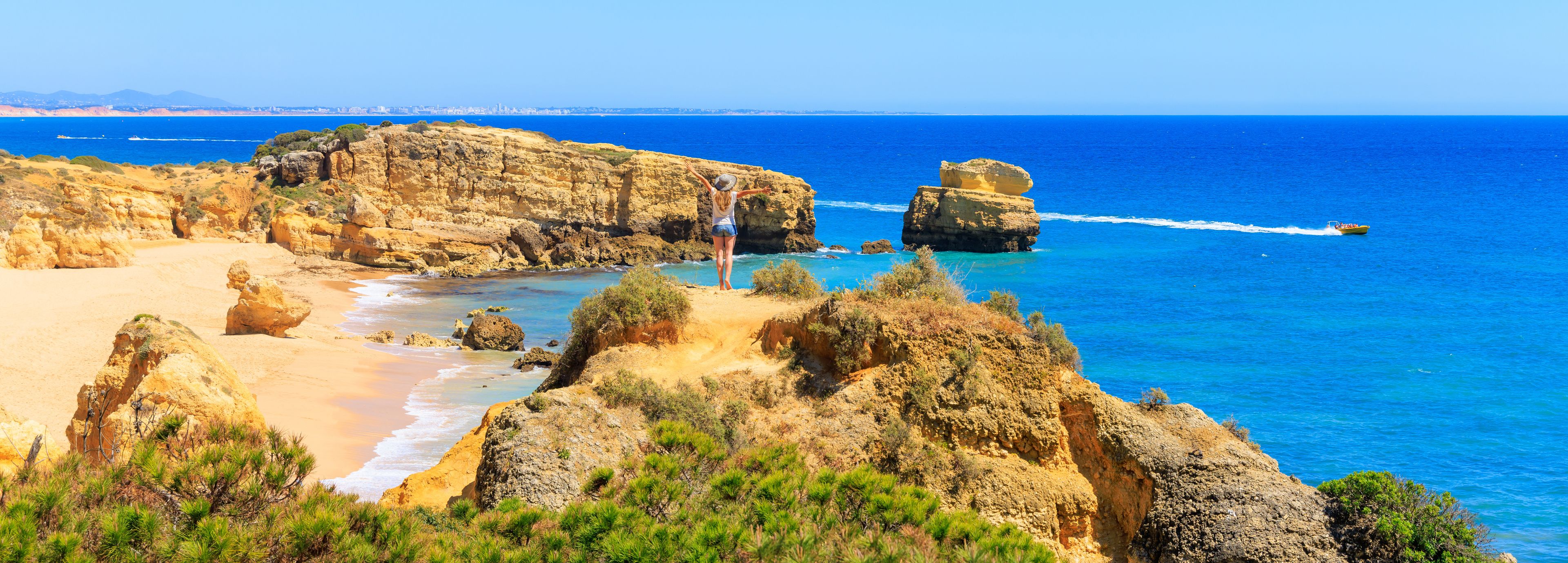 A coastal landscape with rocky cliffs, a sandy beach, and clear blue sea.