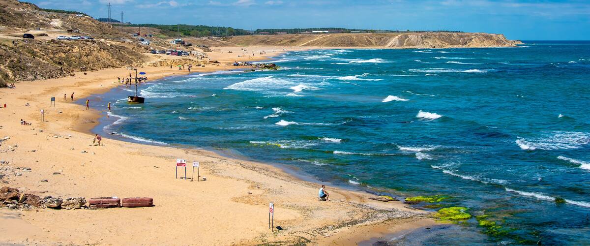 A beach with waves, a sandy shore, and a cliff.