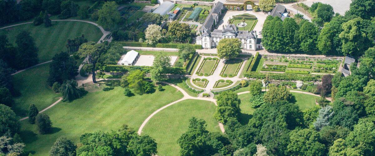 An aerial view of a large estate with manicured gardens, a central building, and surrounding fields.