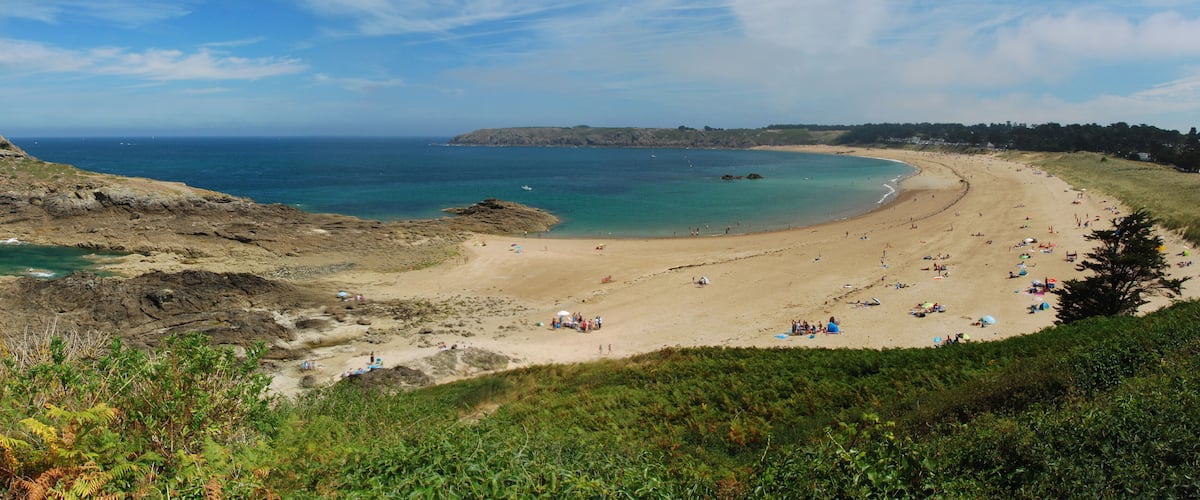 A coastal landscape with a sandy beach, rocky cliffs, and a clear blue sea.