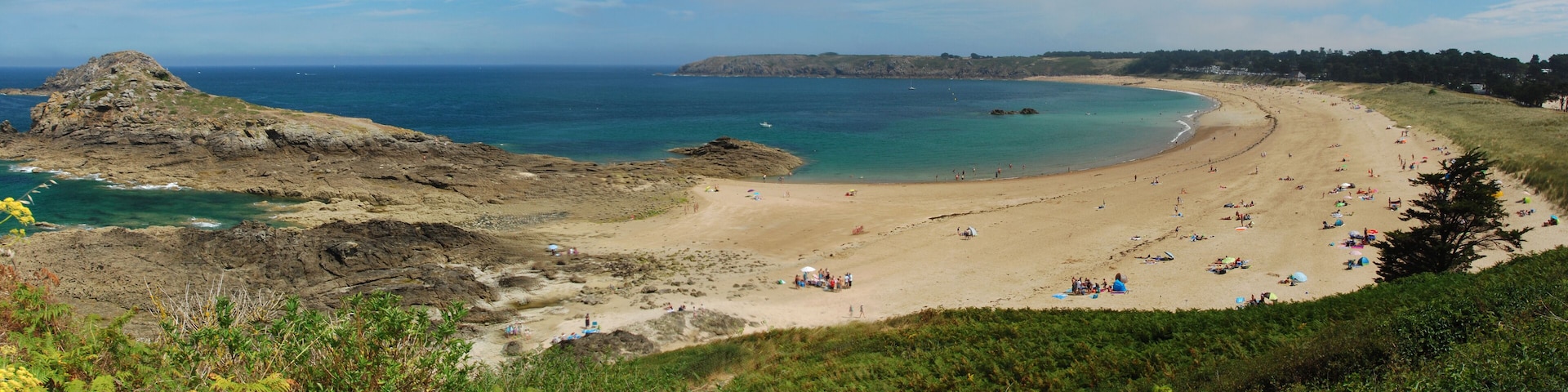 A coastal landscape with a sandy beach, rocky cliffs, and a clear blue sea.
