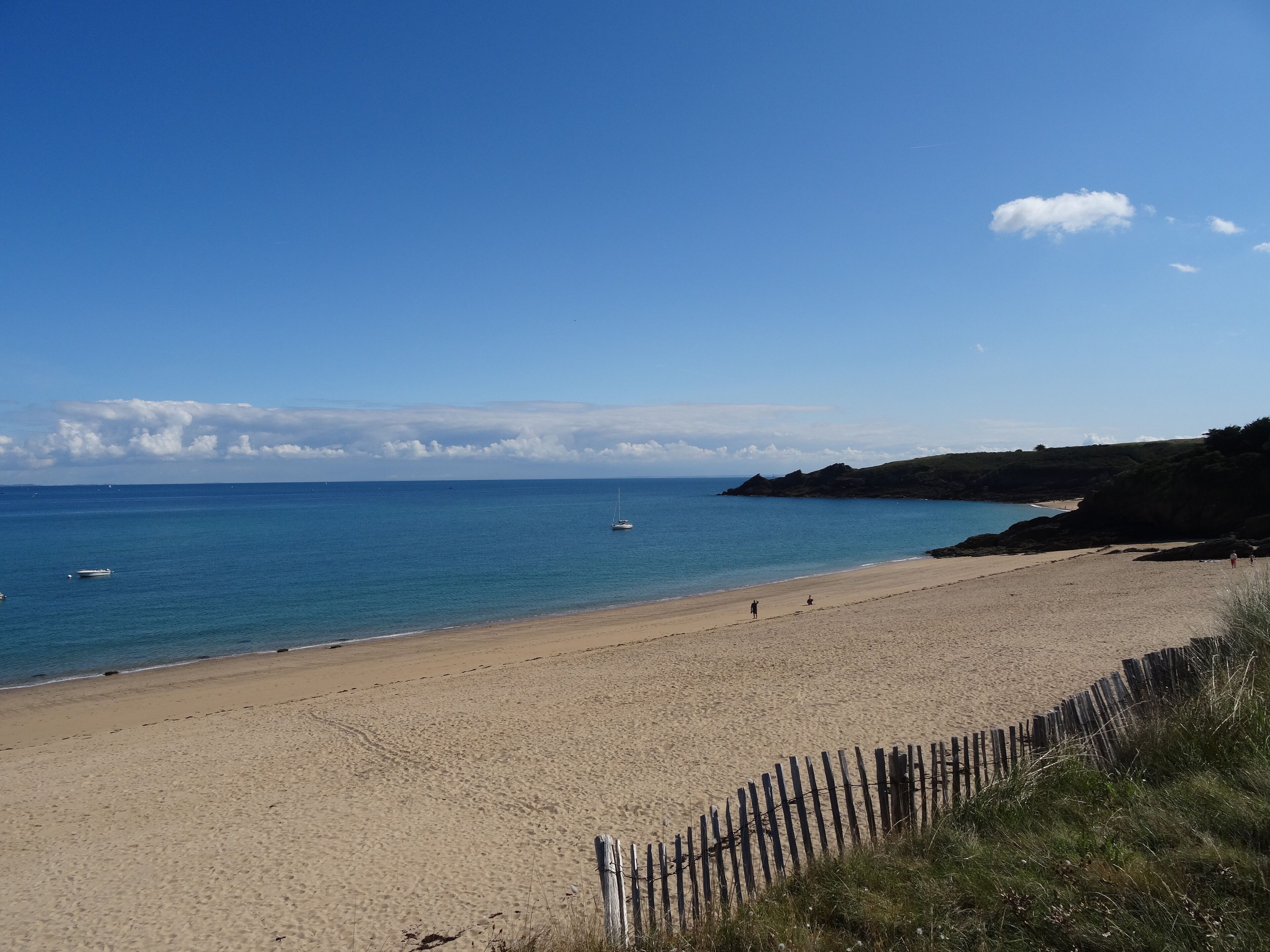 A sandy beach with a wooden fence, calm sea, and a clear sky.