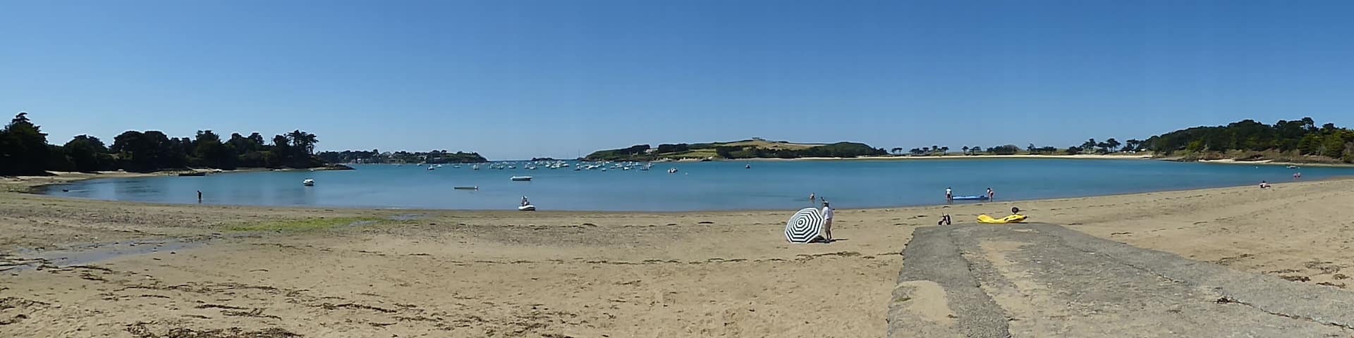 A sandy beach with calm water, boats, and a clear sky.