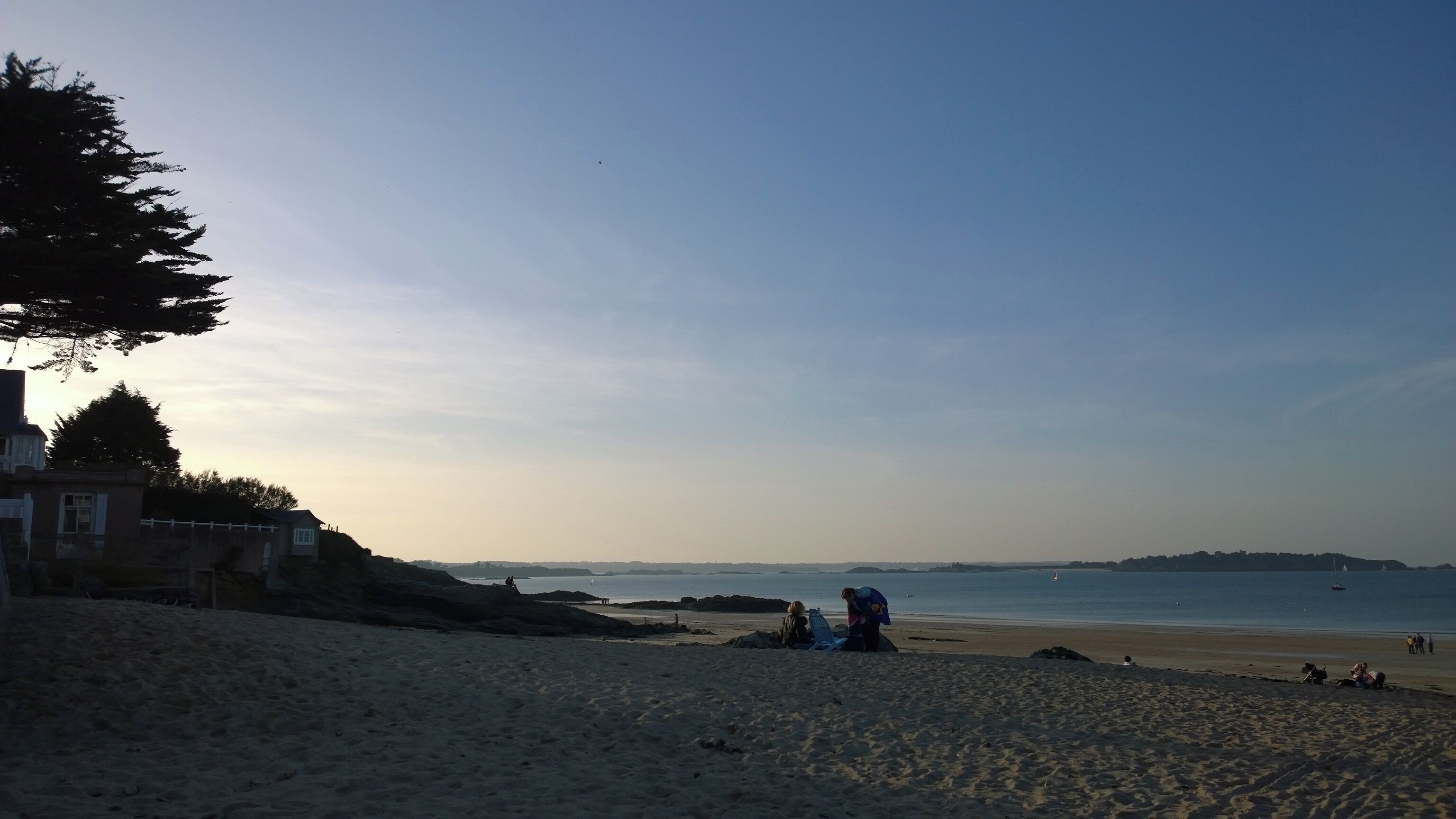 A beach with people, a lighthouse, and a clear sky.