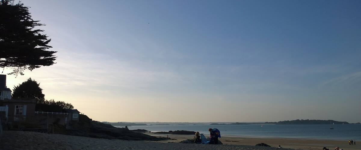 A beach with people, a lighthouse, and a clear sky.