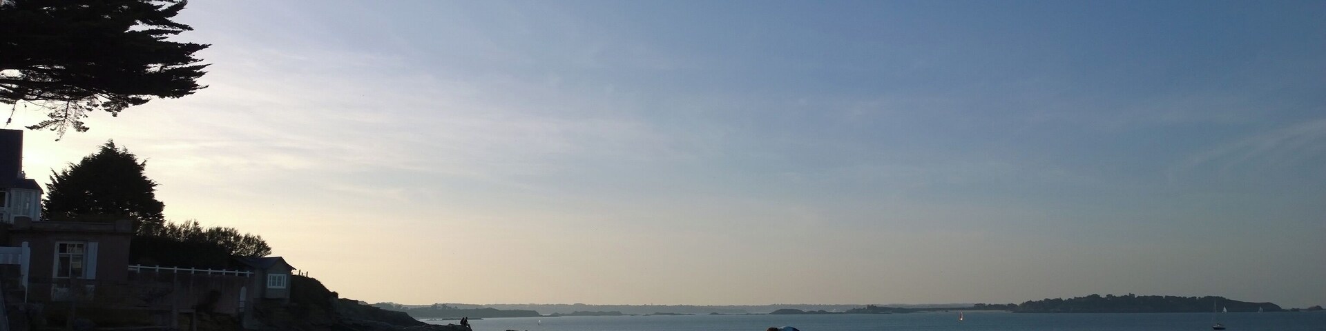 A beach with people, a lighthouse, and a clear sky.
