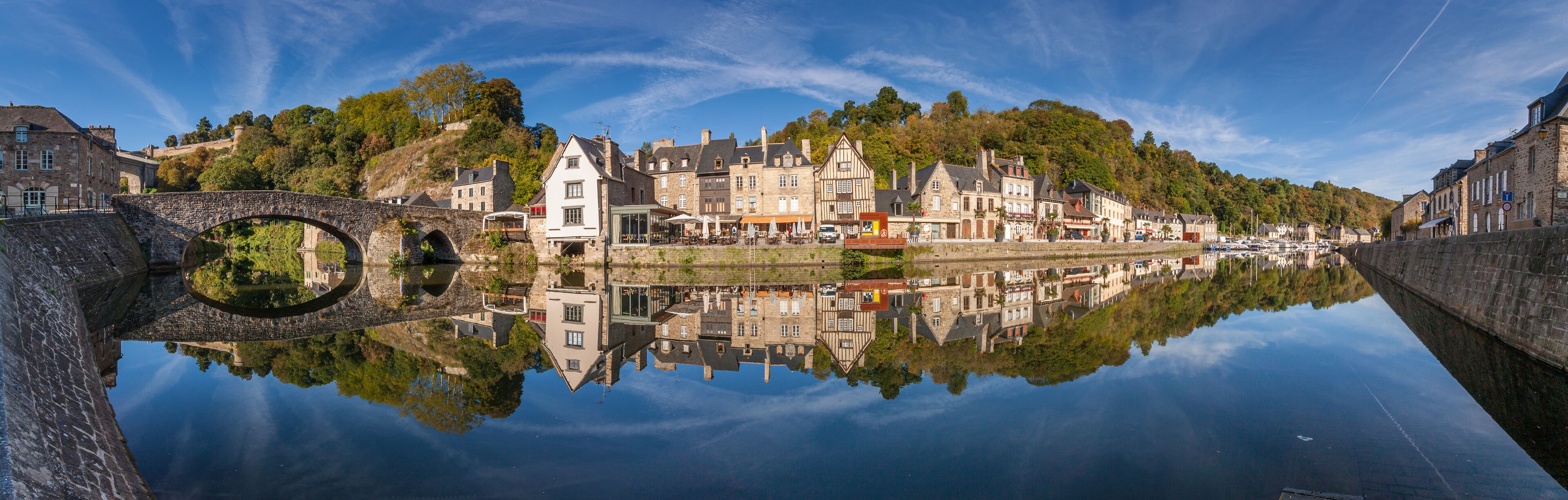 A historic town with a stone bridge over a calm river, reflecting the buildings and lush greenery.