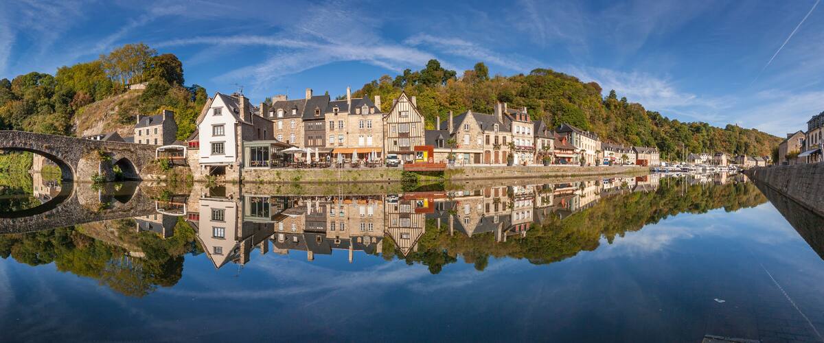 A historic town with a stone bridge over a calm river, reflecting the buildings and lush greenery.