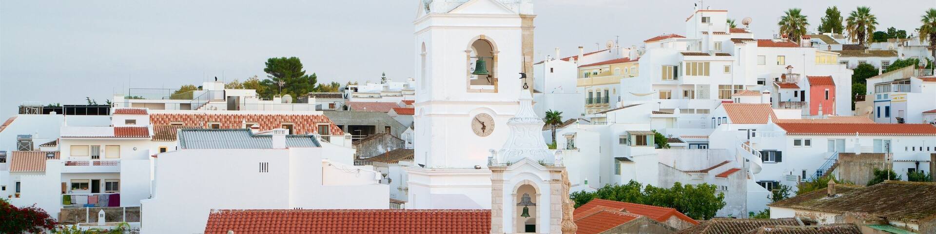 A white church with a bell tower and a clock, surrounded by white buildings with red-tiled roofs.