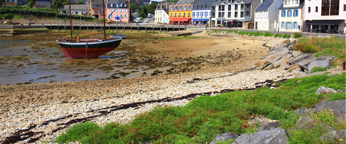 A coastal town with colorful buildings, a red boat on the shore, and a rocky beach.