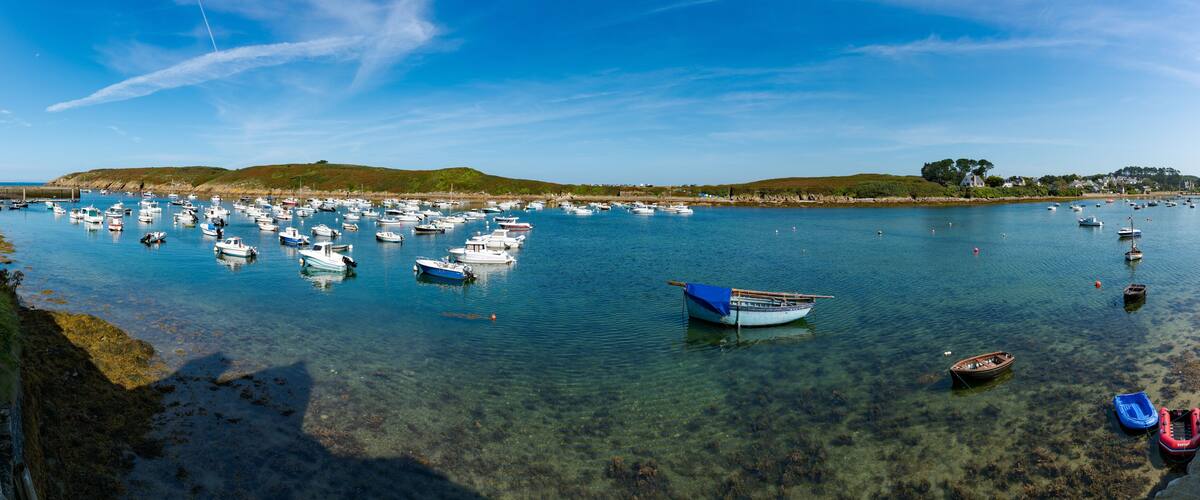 A harbor with numerous boats, clear water, and a hilly landscape in the background.