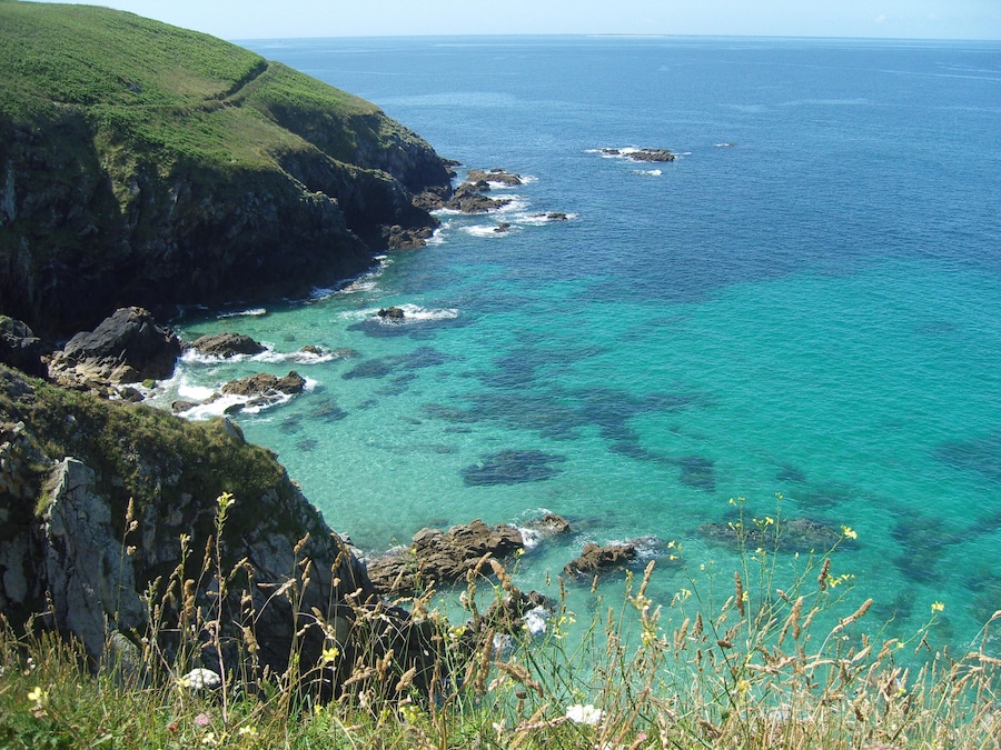 A coastal landscape with clear turquoise waters, rocky cliffs, and green vegetation.