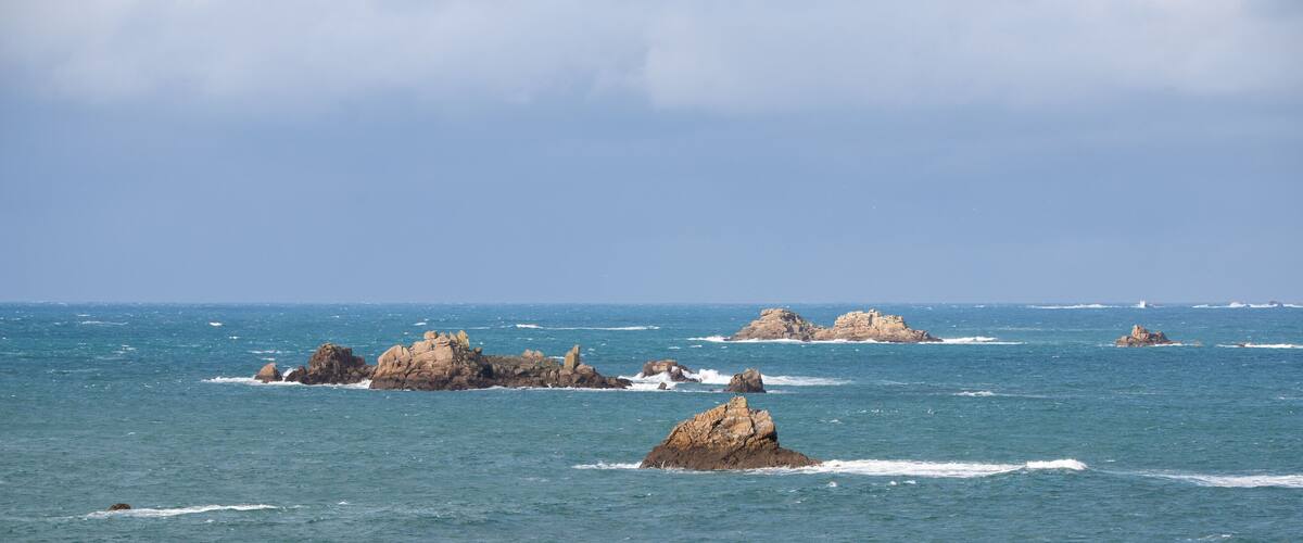 A coastal landscape with rocky outcrops in the sea under a cloudy sky.