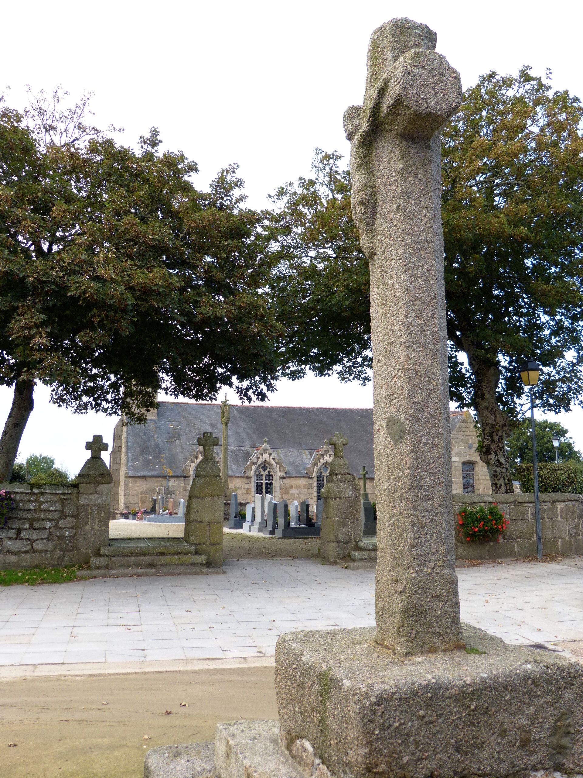 A stone cross in a cemetery with a church in the background.