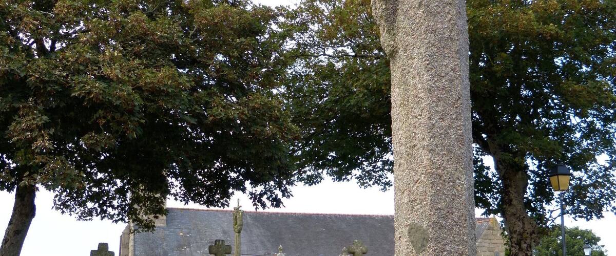 A stone cross in a cemetery with a church in the background.