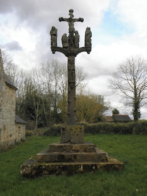 Una cruz de piedra con una escena de crucifixión, rodeada de hierba y árboles.