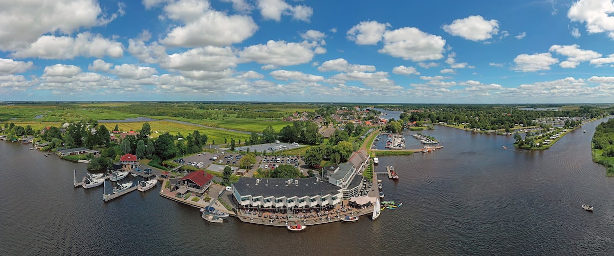 A riverside town with a marina, boats, and a large building with a red roof.