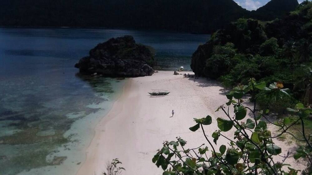 A beach with clear water, a boat, and rocky formations.