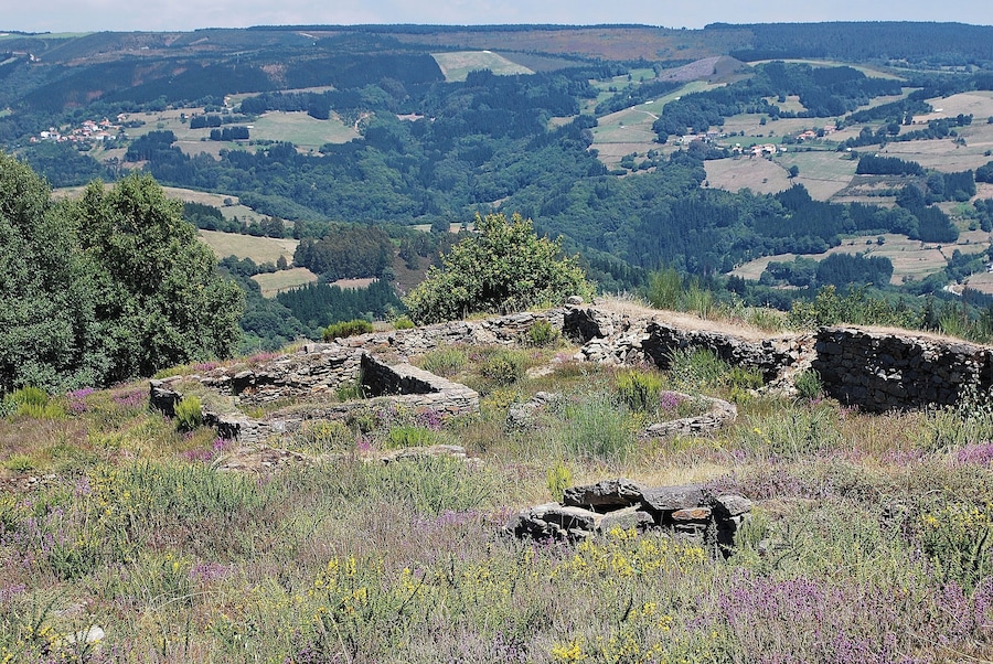 A stone ruin amidst a lush valley with rolling hills and scattered houses.