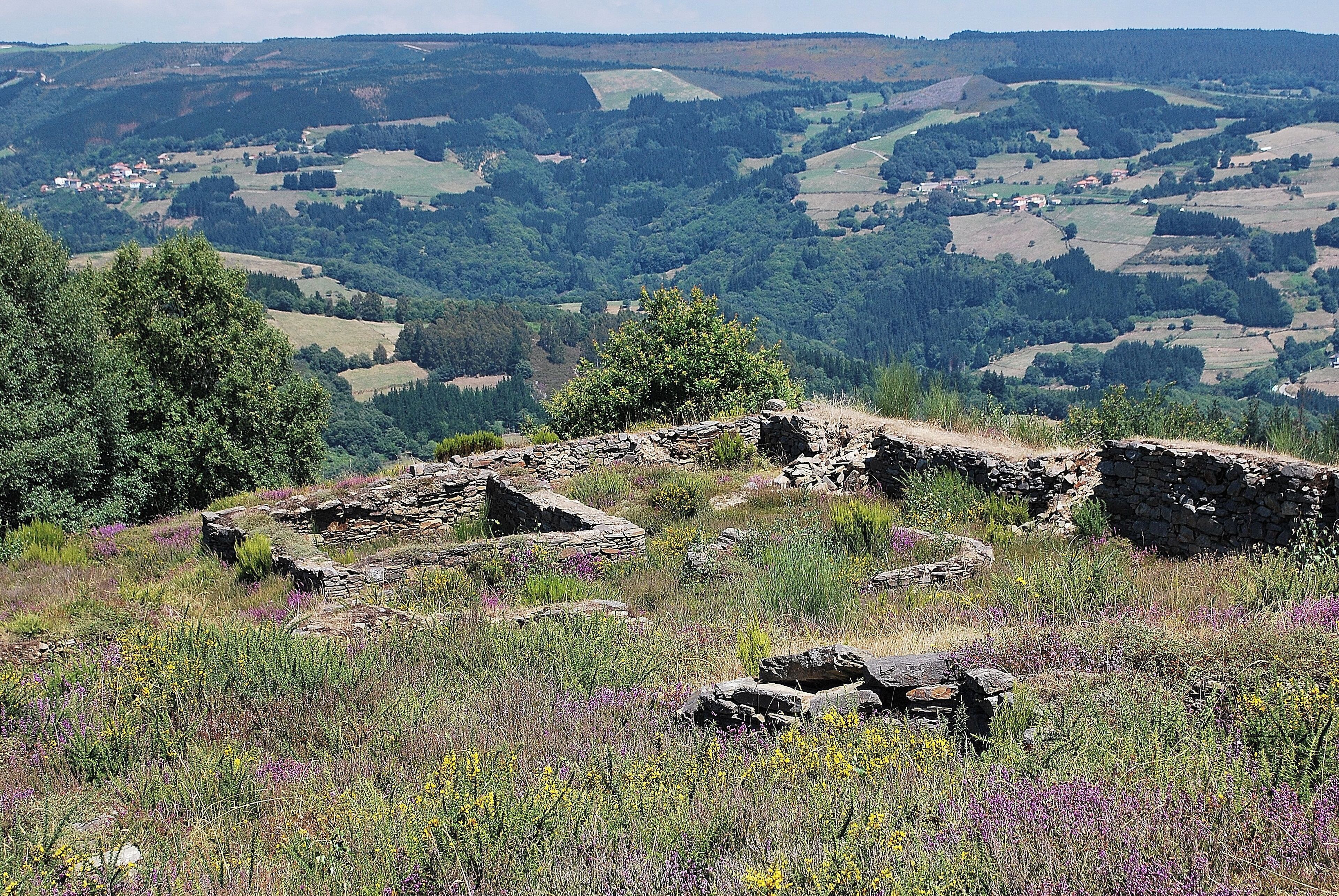 A stone ruin amidst a lush valley with rolling hills and scattered houses.