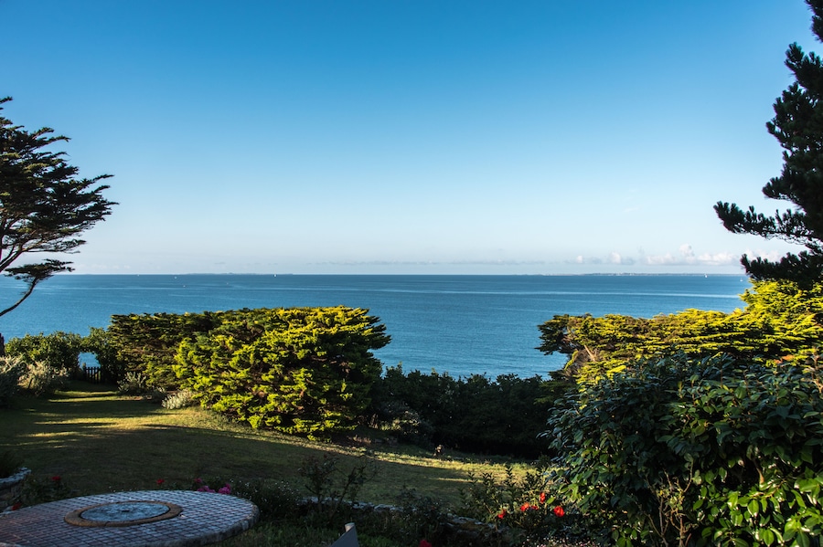 Paisagem costeira com vista clara do mar, silhueta distante da cidade e vegetação exuberante.