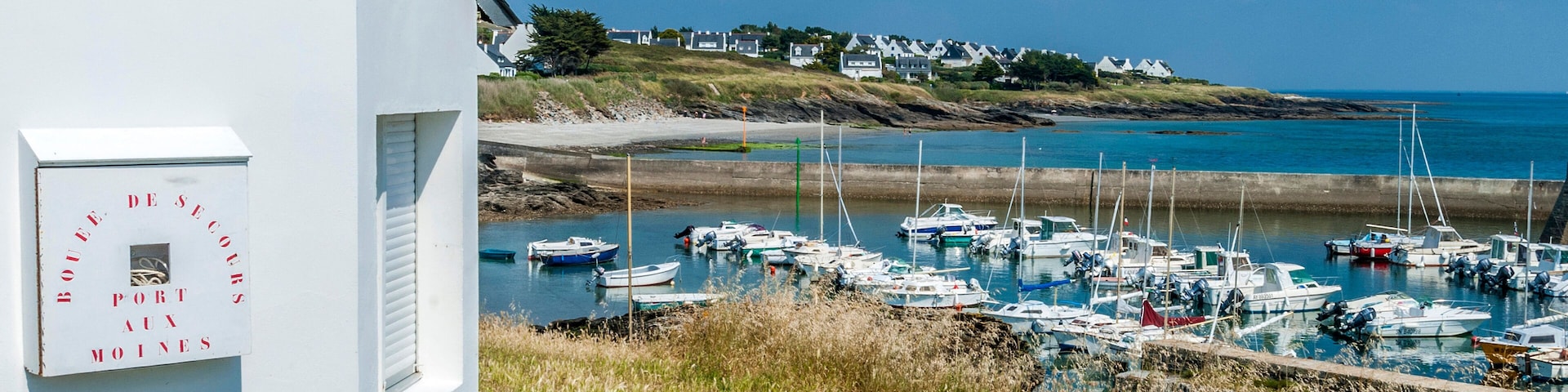 Un edificio blanco con un cartel que dice "BOULDEURS PORT AUX MOINES" que domina un puerto deportivo con barcos.