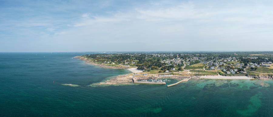 Vue aérienne d’une ville côtière avec un port de plaisance, des plages de sable et des quartiers résidentiels.