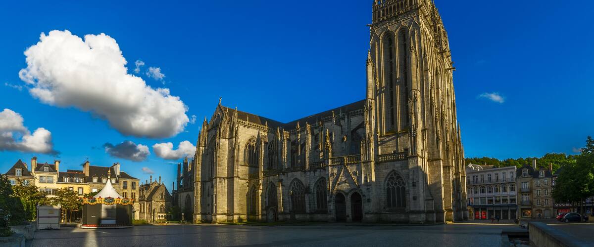 A Gothic cathedral with a tall spire, surrounded by historic buildings and a clear blue sky.
