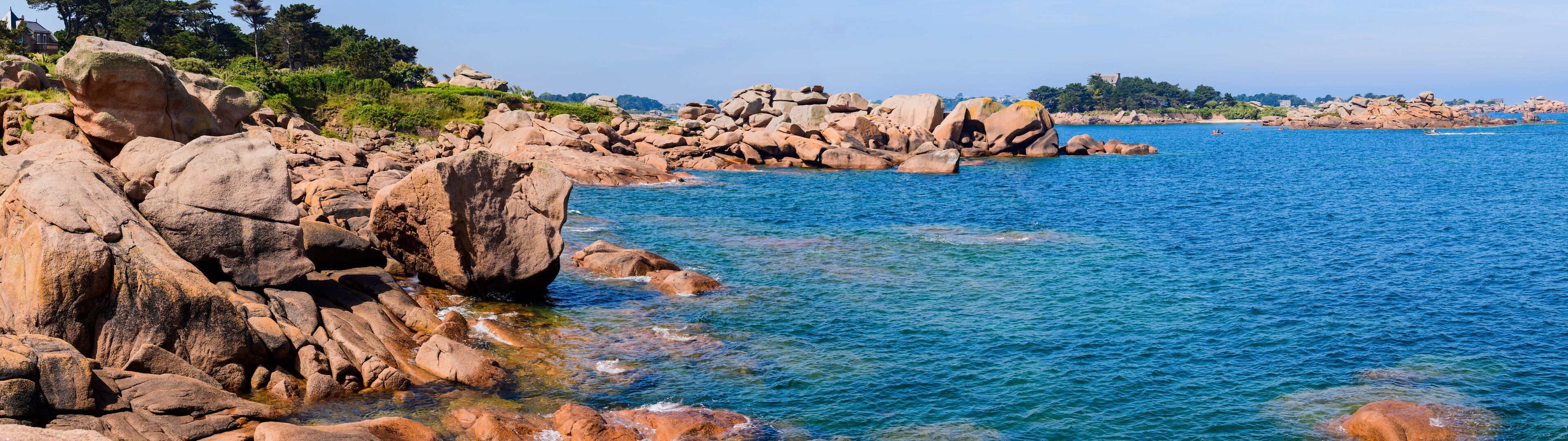 A rocky coastline with clear blue water and distant buildings.