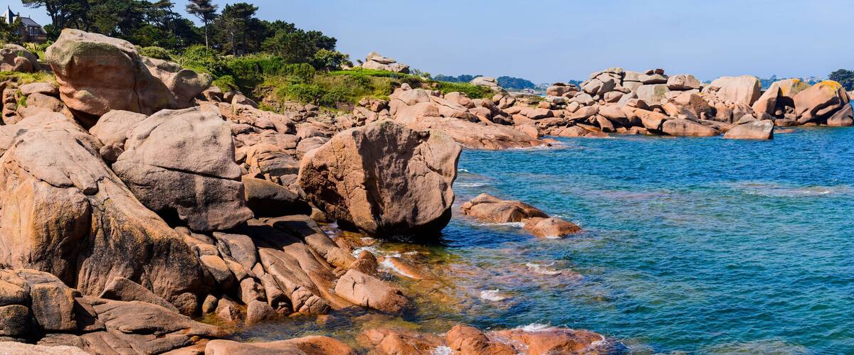 A rocky coastline with clear blue water and distant buildings.