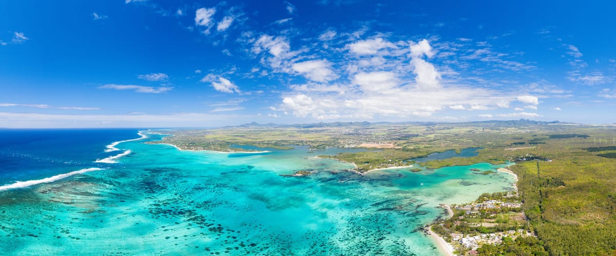 A coastal landscape with turquoise waters, a sandy beach, and a distant mountain range.