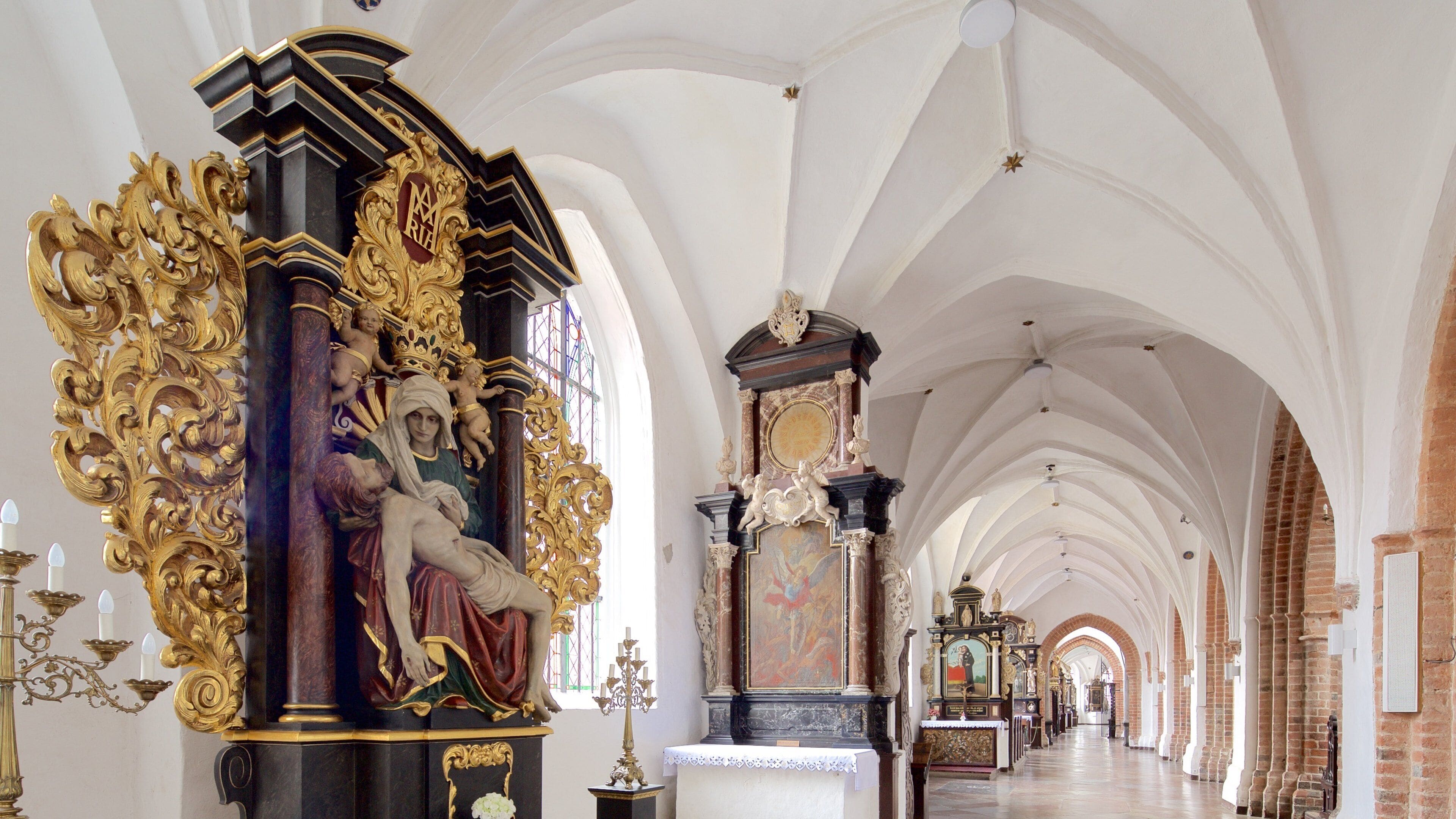 An ornate church interior with high vaulted ceilings, golden decorations, and religious statues.