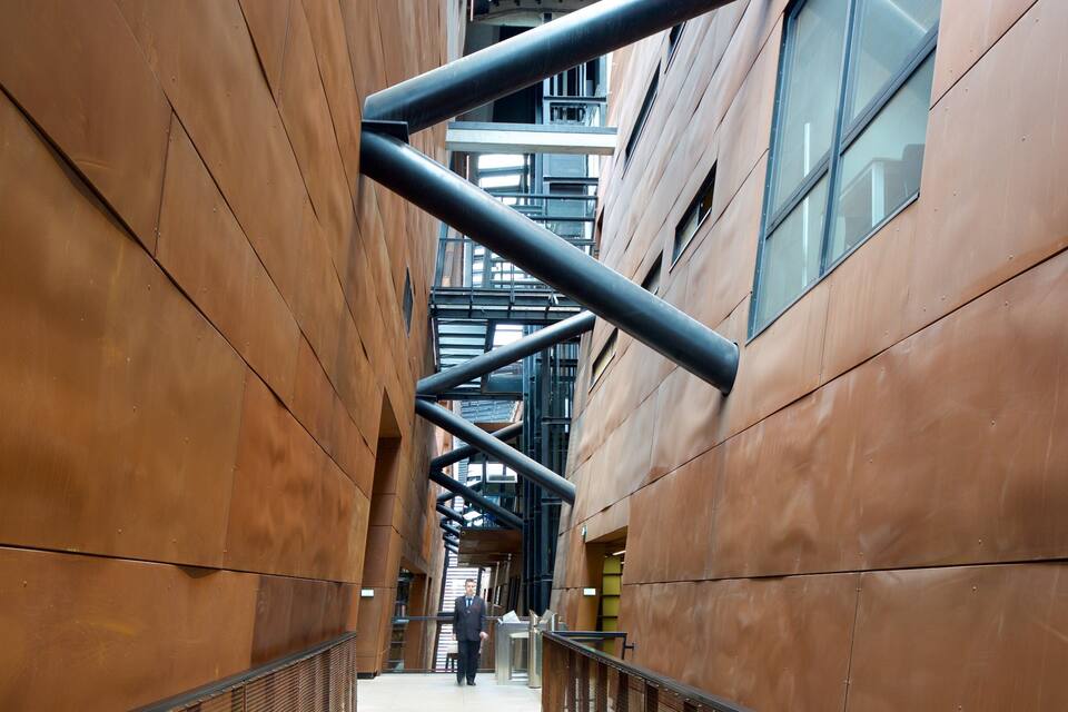 Un couloir au design architectural moderne, avec une allée centrale bordée de grands panneaux métalliques bruns et d’éléments structurels noirs.