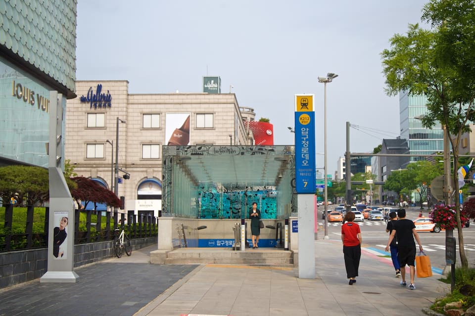 A city street with a modern building, a glass structure with graffiti, and a metro station entrance.