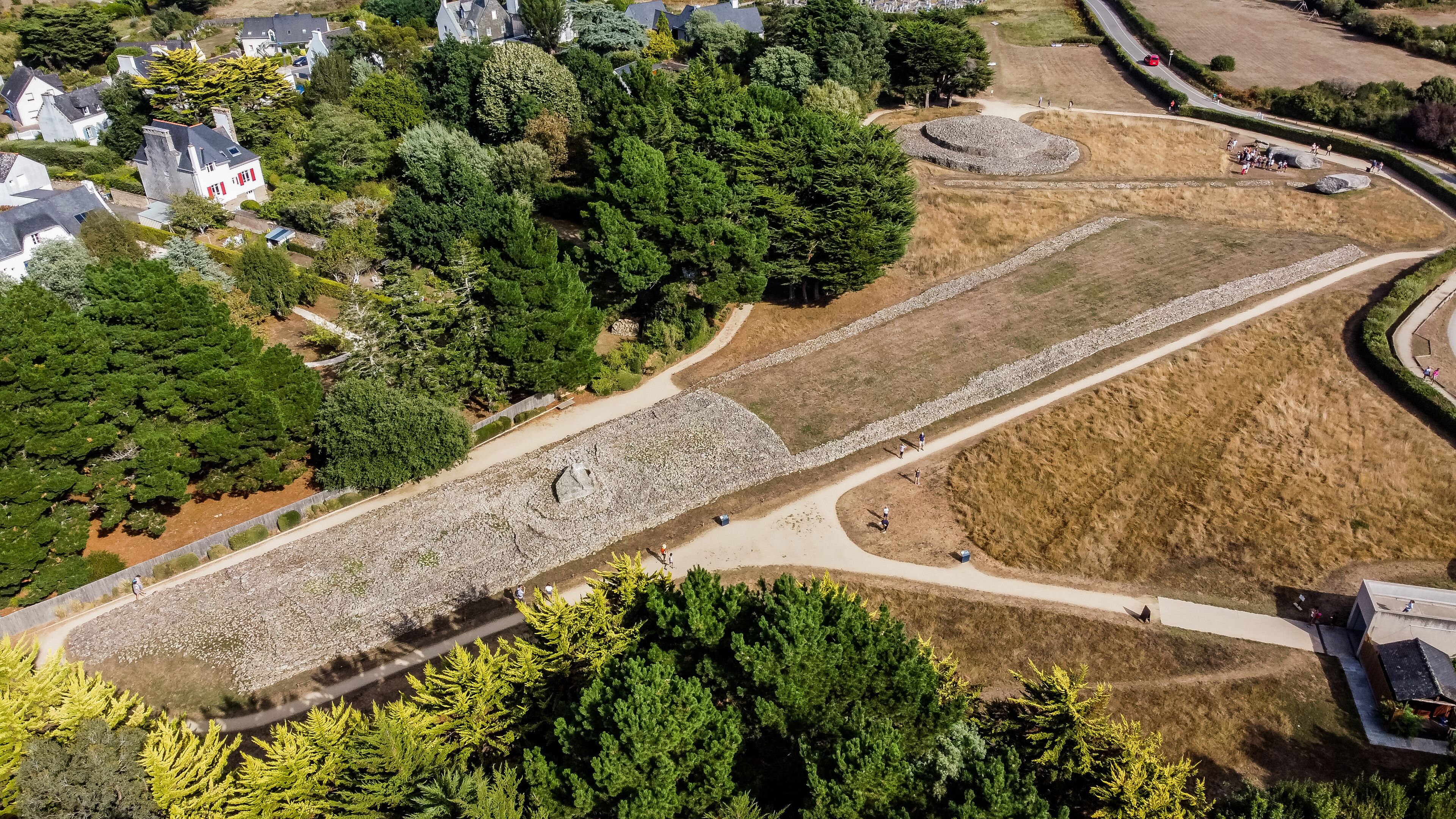 An aerial view of a residential area with houses, a winding road, and a large open field with a stone wall.