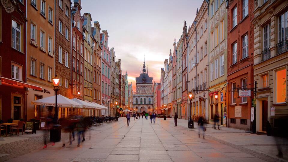 A bustling European street with colorful buildings, outdoor cafes, and a prominent church spire in the background.