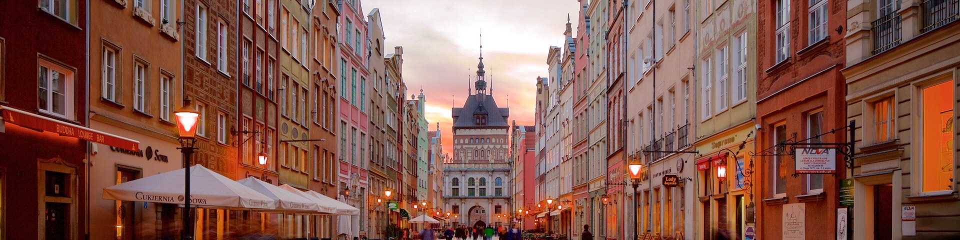 A bustling European street with colorful buildings, outdoor cafes, and a prominent church spire in the background.