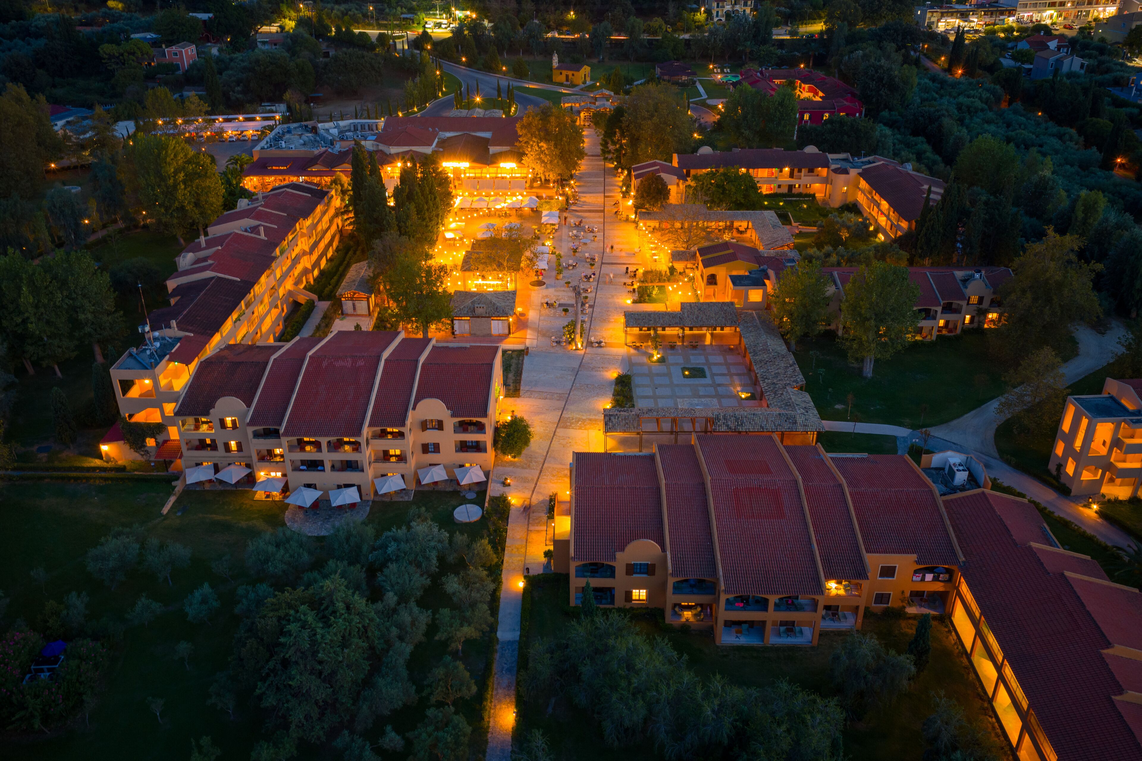 Wide aerial panorama of the sprawling Grecotel Costa Botanica luxury resort in Corfu, Greece, illuminated against the twilight sky