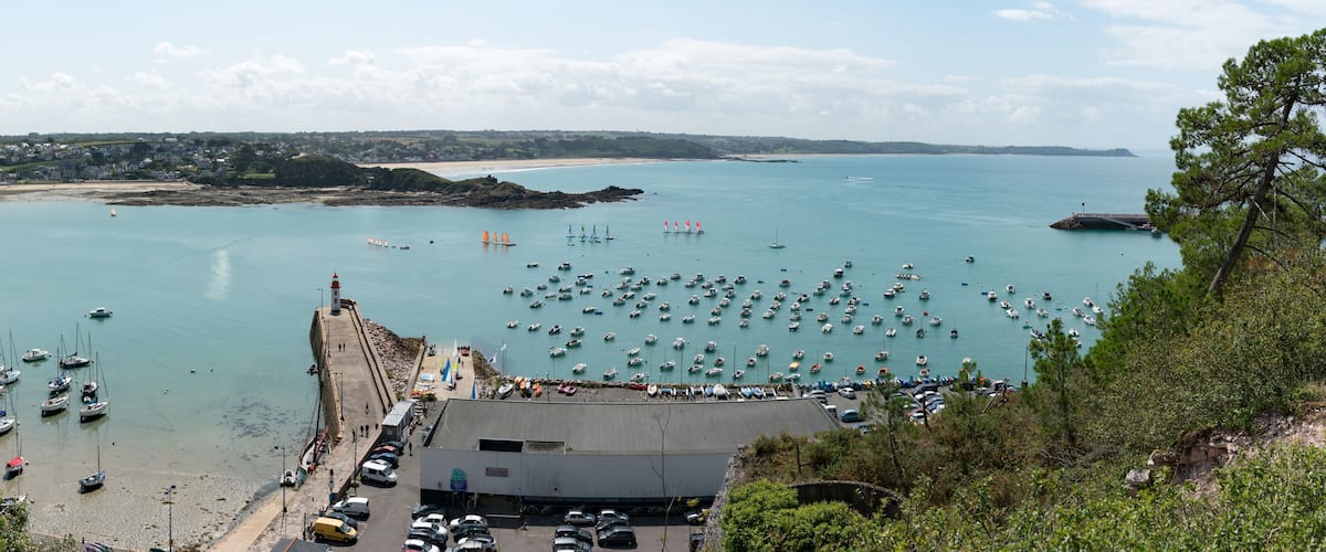 A coastal town with a marina filled with boats, a lighthouse, and a beach.