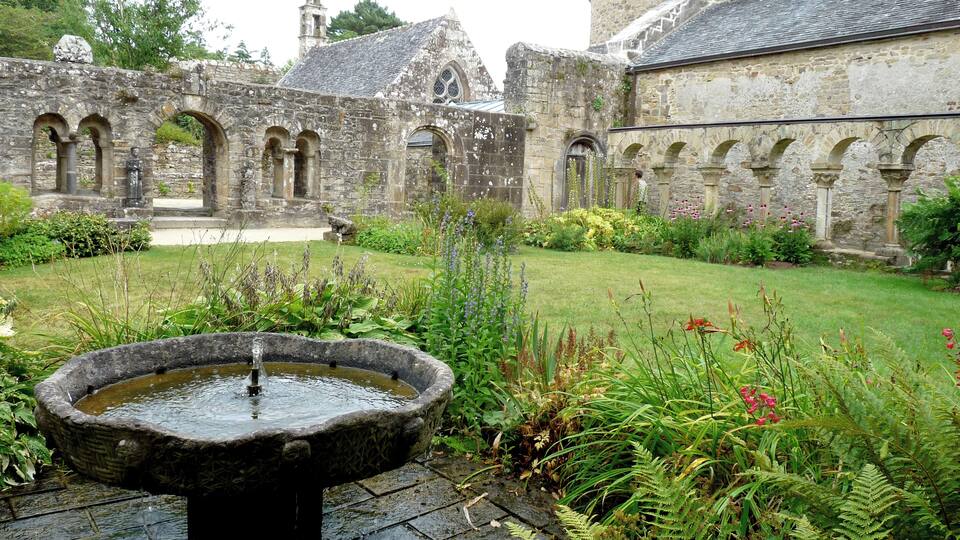 A historic stone building with arched windows and a fountain in a garden.