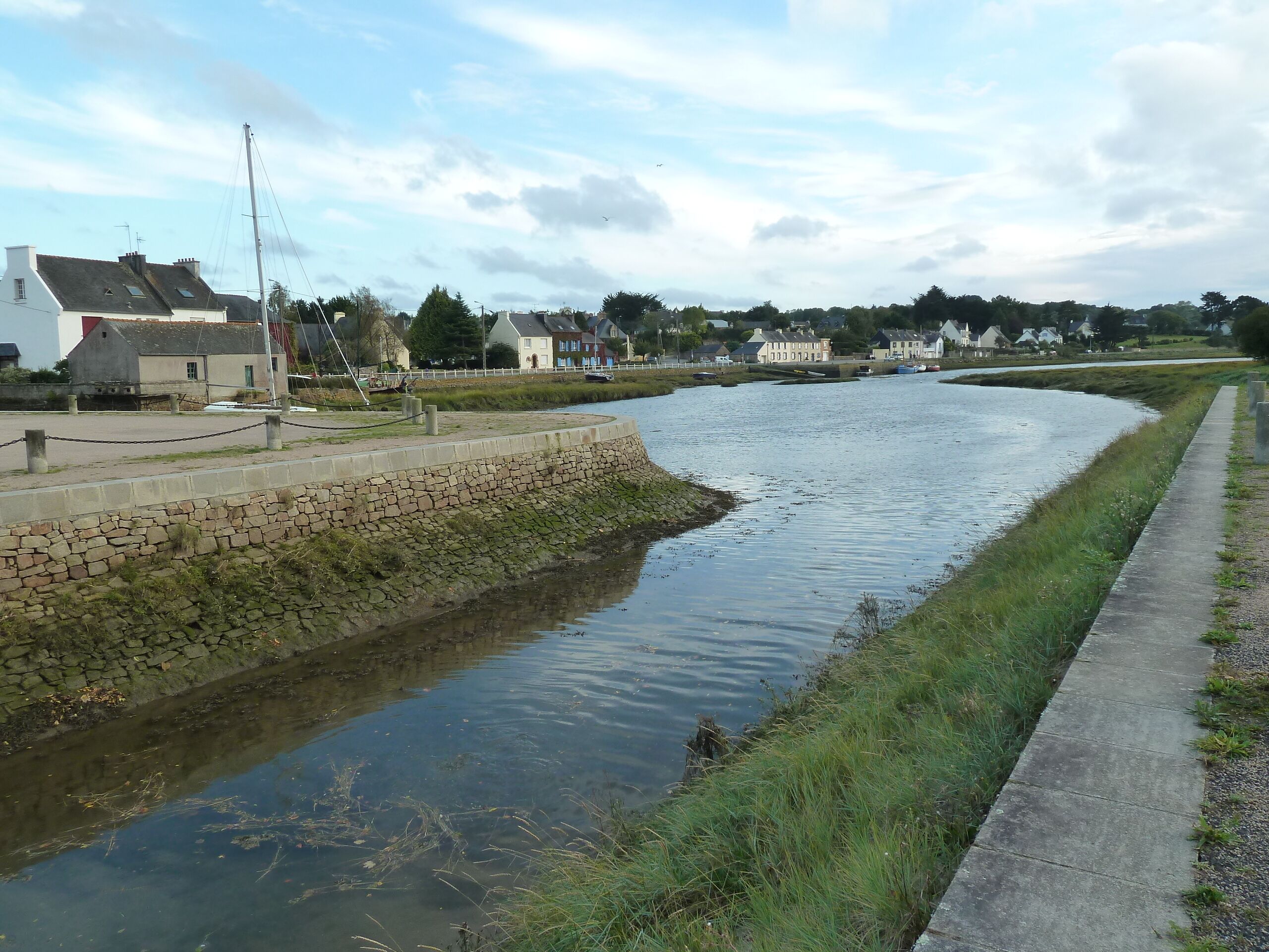 A calm river with a stone embankment and a grassy path alongside.