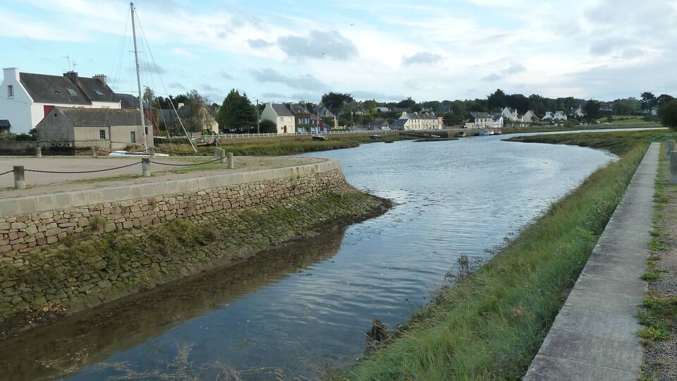 A calm river with a stone embankment and a grassy path alongside.