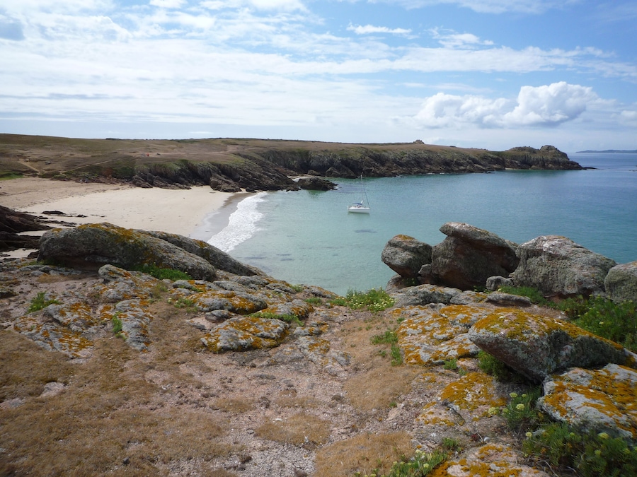 Paisaje costero con playa arenosa, afloramientos rocosos y un pequeño bote en el agua.
