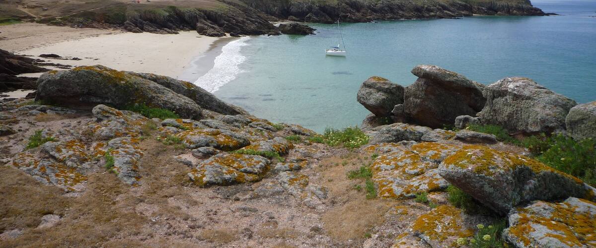 A coastal landscape with a sandy beach, rocky outcrops, and a small boat on the water.