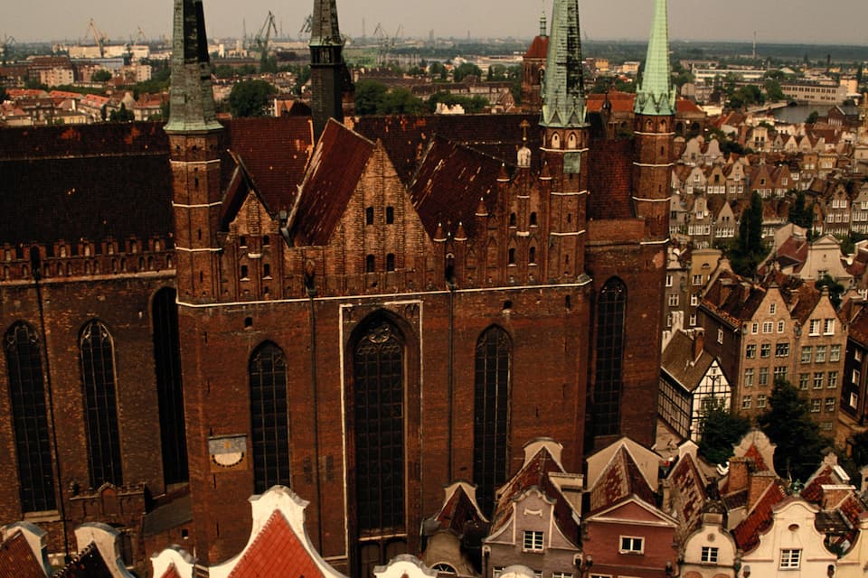 A historic church with multiple spires and a red-tiled roof amidst a densely packed urban area.