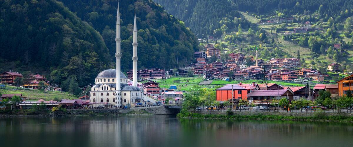 A mosque with two minarets, a lake, and a mountainous backdrop.