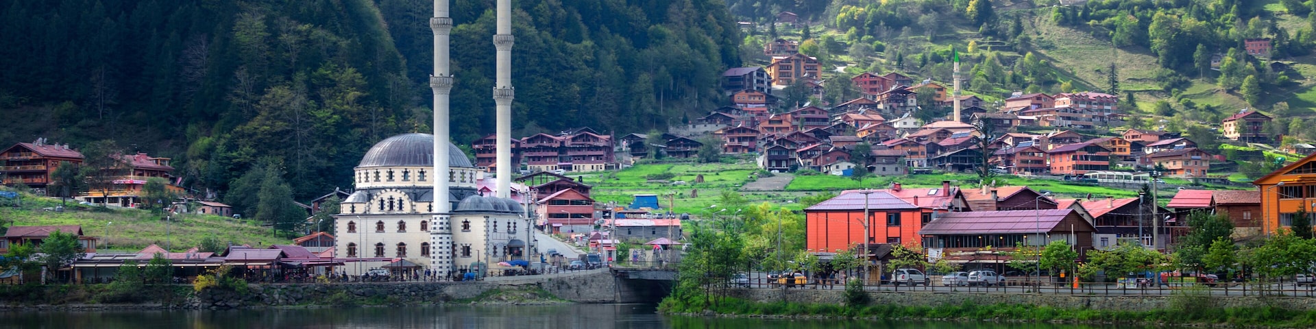 A mosque with two minarets, a lake, and a mountainous backdrop.