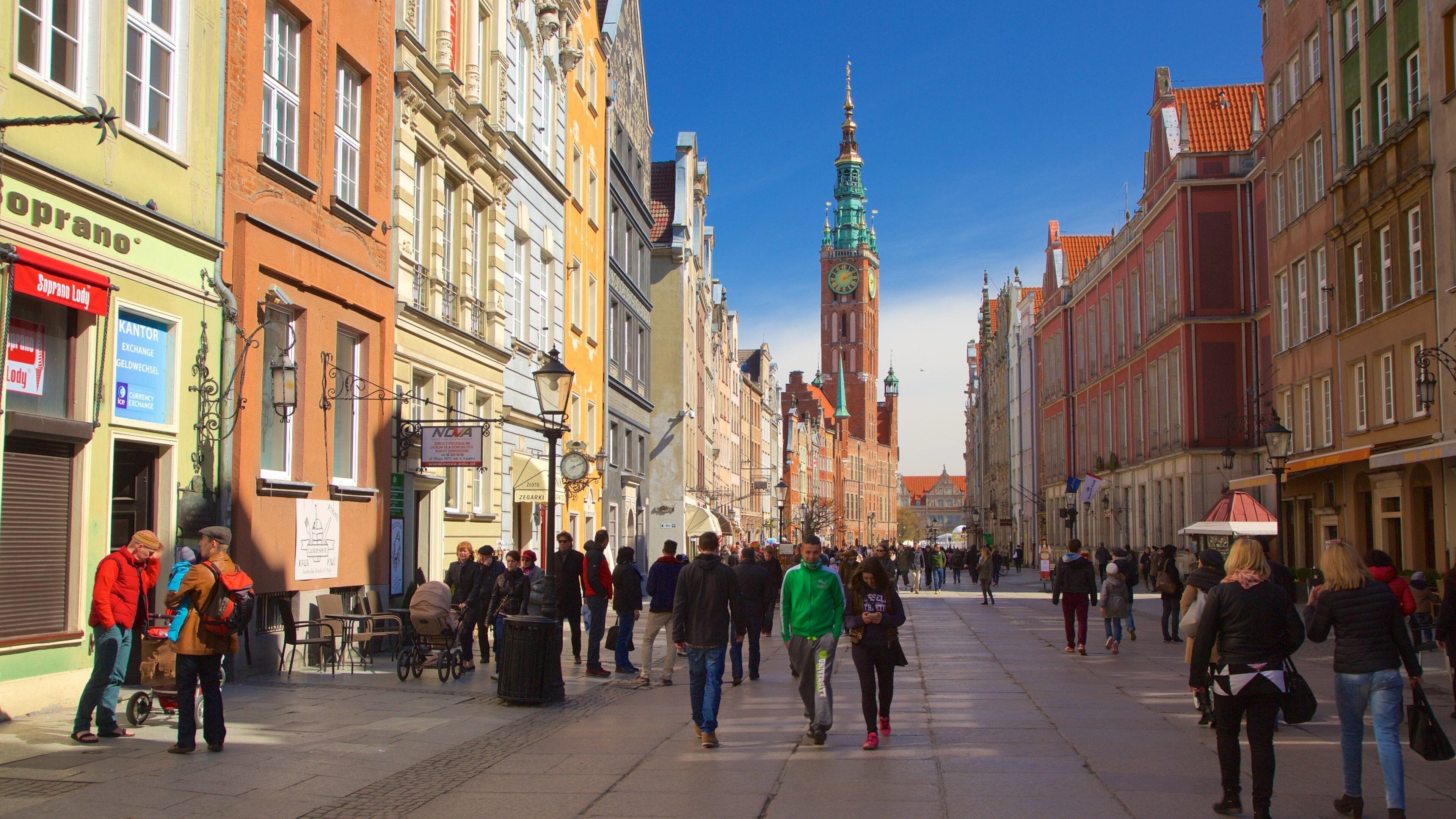Una vivace strada con edifici storici, un'imponente torre dell'orologio e persone che camminano.